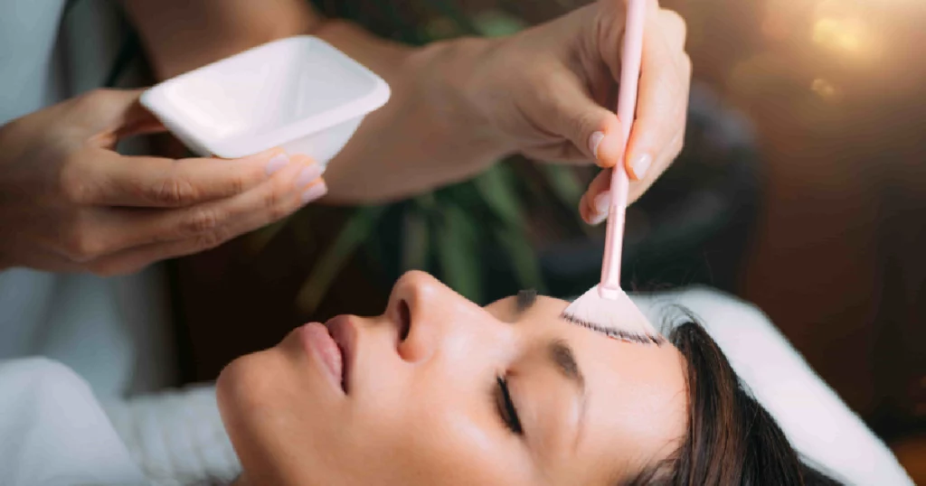 A woman with closed eyes receives a chemical peel treatment as a professional applies solution to her forehead with a brush in a spa setting in Richmond, KY